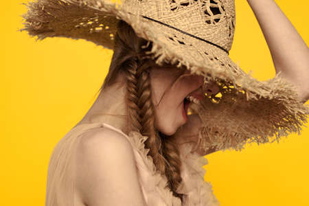 Portrait of a pretty woman with pigtails and with a hat on her head on a yellow background cropped...
