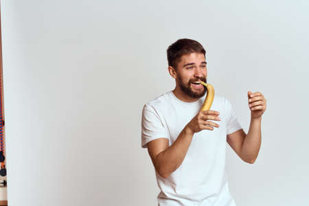 Cheerful man with a banana in his hands on a light background fun emotions Cropped view Copy Spaceの写真素材
