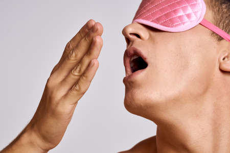 A man in a pink mask for sleeping on a light background at night gestures with his hands