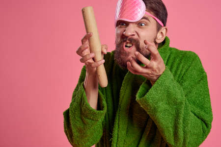 Portrait of a man in a pink sleep mask and a wooden rolling pin emotions green robe irritability modelの写真素材