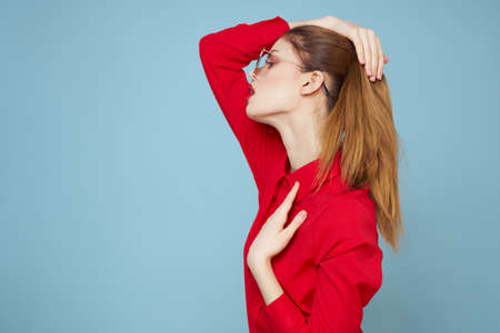 Woman in red shirt on blue background holds hands near face and sunglasses red lips makeup modelの写真素材