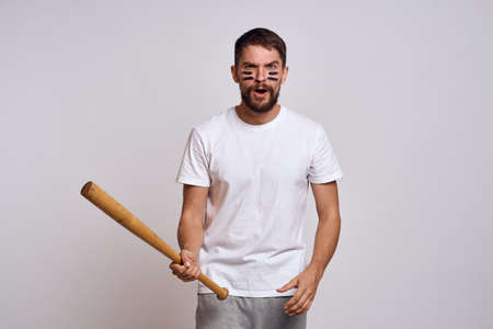 An emotional man with a baseball bat on a light background in a white T-shirt is gesturing with his hands to the modelの写真素材