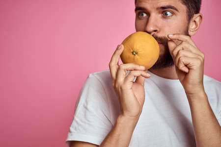Young man with orange on a pink background in a white t-shirt emotions fun gesticulating with model handsの写真素材