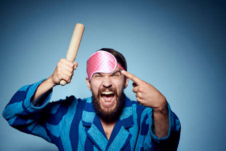 man with rolling pin and in pink sleep mask blue robe cropped view emotion modelの写真素材