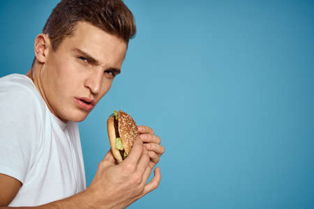 man with hamburger and white t-shirt blue background emotions gesturing with hands Copy Spaceの写真素材