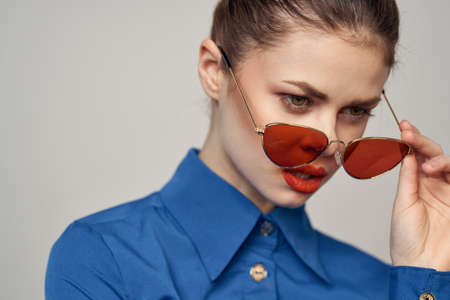 Fashionable woman in sunglasses and a blue shirt gesturing with her hands on a light background...