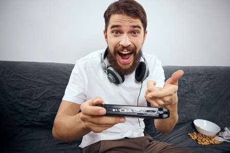 A man sits on a sofa with a gamepad in his hand. Leisure lifestyle game console