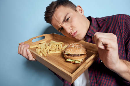 Man with wooden pallet fast food french fries hamburger hunger diet food blue backgroundの写真素材