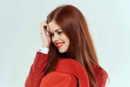 Elegant woman in red jacket hat holding long hair cropped light background