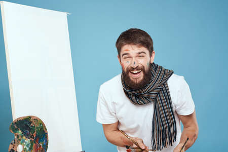 Male artist with palette brush easel on blue backgroundの写真素材