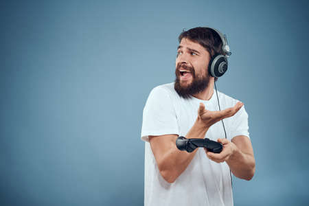 Man in headphones controller in hands playing game console lifestyle emotions blue background white t-shirtの写真素材