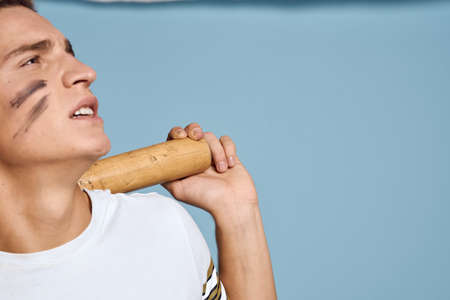 baseball guy with a bat in his hand on a blue background and a combat color on his face makeup model...
