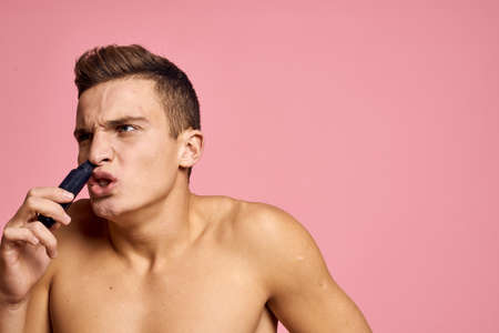 Handsome man with a trimmer in his hand hair removal machine pink background naked torso