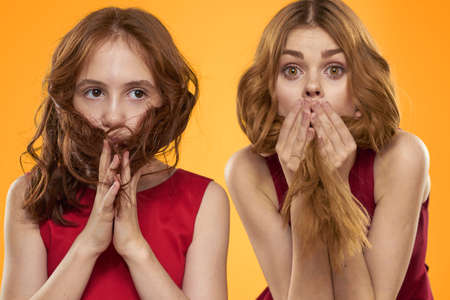 A red-haired girl and a beautiful woman on a yellow background in red dresses gesticulate with their...