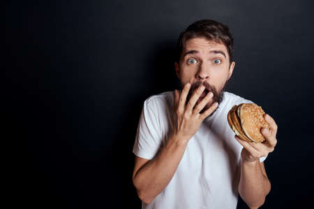 Man eating hamburger fast food restaurant Gourmet eating dark backgroundの写真素材