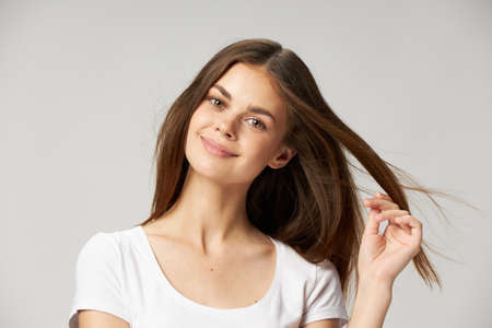 A woman in a white T-shirt touches the hair on her head with her hand on a light backgroundの写真素材