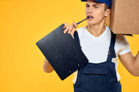 Working man in uniform with box hand delivery loading service yellow backgroundの写真素材