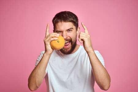 Young man with orange on a pink background in a white t-shirt emotions fun gesticulating with model...