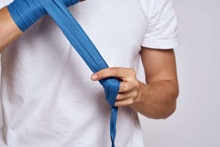 A man ties his hand with boxing bandages in a white T-shirt
