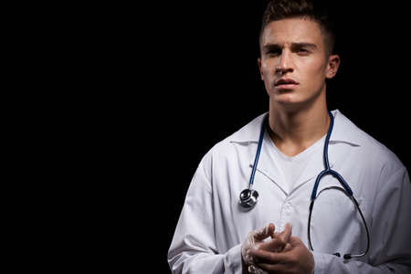 professional doctor in a medical gown with a stethoscope around his neck against a dark background cropped viewの写真素材