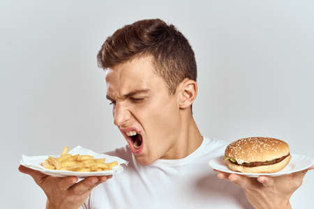 a man with fries and a hamburger on a light background in white t-shirt close-up cropped view Copy Space Modelの写真素材