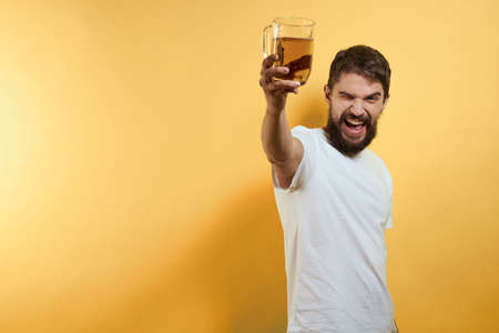 Man with a mug of beer fun alcohol lifestyle white t-shirt yellow isolated backgroundの写真素材