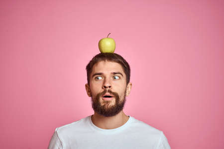 Cute man with an apple on a pink background gestures with his hands cropped white T-shirt Copy Space