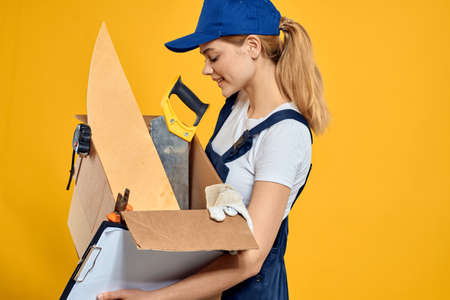 Woman with a box of construction tools and in a cap on a yellow background repair construction...