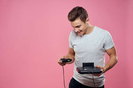 Cute man console in hands of video game entertainment lifestyle gray t-shirt pink backgroundの写真素材