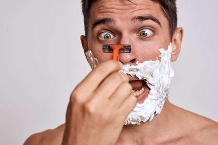 Handsome man with white shaving foam on his face and clean skin with razor grooming bare shouldersの写真素材