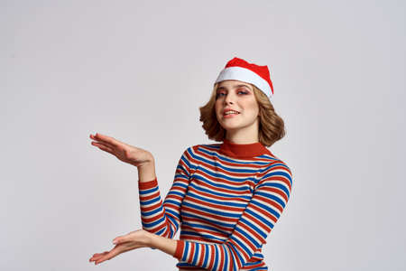 Happy woman in a Christmas cap and a striped sweater gestures with her hands for the New Year holidaysの写真素材