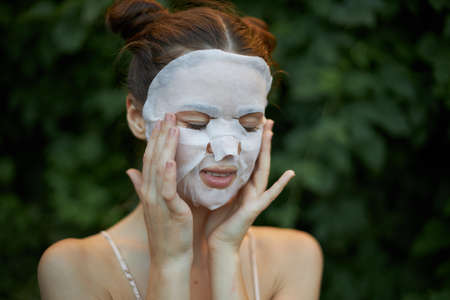Beautiful woman With his eyes closed, touches his face with his hands white mask skin careの写真素材