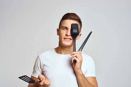 Guy with kitchen tools in hands on a light background cropped view of emotions fun modelの写真素材
