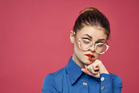 Portrait of a woman in glasses and in a blue shirt red lips pink background modelの写真素材