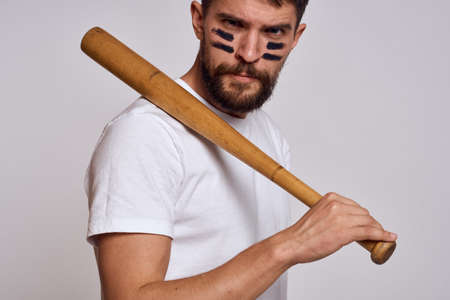 An emotional man with a baseball bat on a light background in a white T-shirt is gesturing with his hands to the modelの写真素材
