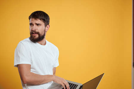 A man with a beard holds a laptop in his hand on a yellow background keyboard monitor new technologies side viewの写真素材