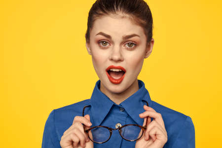 Portrait of a woman with glasses in her hands on a yellow background and in a blue shirt cropped...