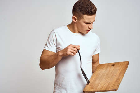 Guy with kitchen tools in hands on a light background cropped view of emotions fun modelの写真素材