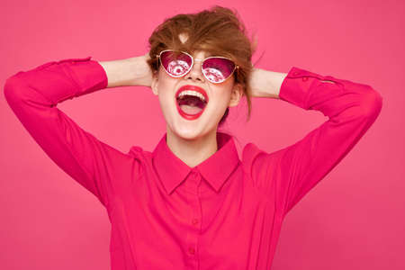 Cheerful woman in sunglasses touching hair with hands and pink shirt cropped viewの写真素材