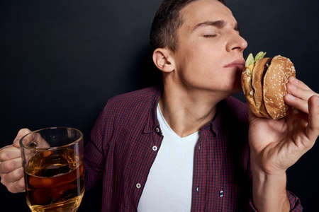 man with beer mug and hamburger in hands fun lifestyle studio dark isolated backgroundの写真素材