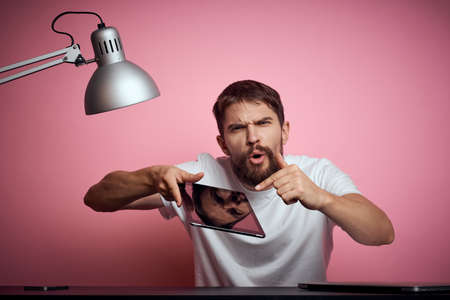 Man working at the table room electric lamp pink background open laptop new technology tablet monitorの写真素材