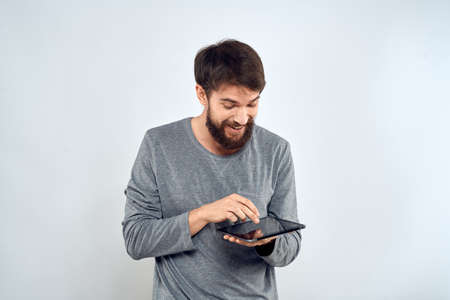 A bearded man with a tablet in his hands a gray jacket technology internet light backgroundの写真素材