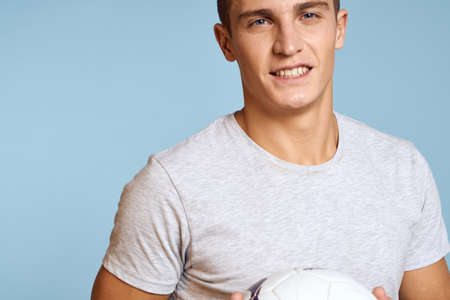 Happy guy with soccer ball in hand on blue background plays soccer cropped view