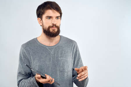 A man in a gray sweater a tablet in the hands of emotions Internet technology lifestyle light backgroundの写真素材