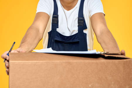 Working man in uniform with box hand delivery loading service yellow backgroundの写真素材
