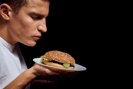 Man with hamburger plates on black background in white t-shirt portrait cropped view of fast foodの写真素材