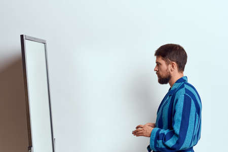a man in a blue robe examines himself in a mirror in a bright room cropped viewの写真素材