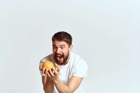 a man with an orange in a white t-shirt on a light background the diet of a brunette thick beard