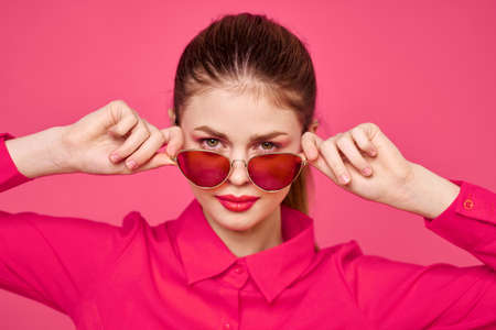Fashion woman in pink shirt with glasses in hands on isolated background cropped viewの写真素材