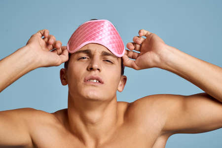 Relaxed man with pink sleep mask on blue background nude torso cropped viewの写真素材